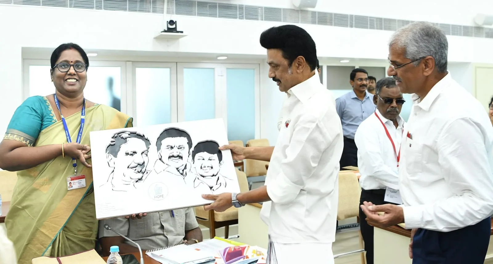 Hope Chennai staff presenting a student's pencil portrait drawing at a government meeting