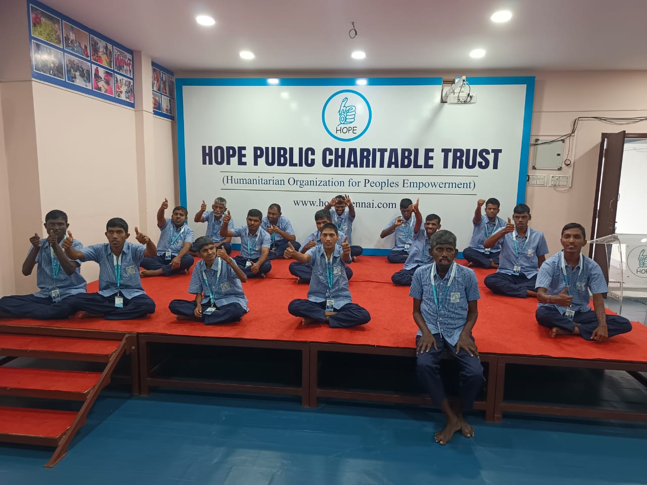 Hope Chennai students seated on the stage in front of the Hope Public Charitable Trust sign, giving a thumbs up
