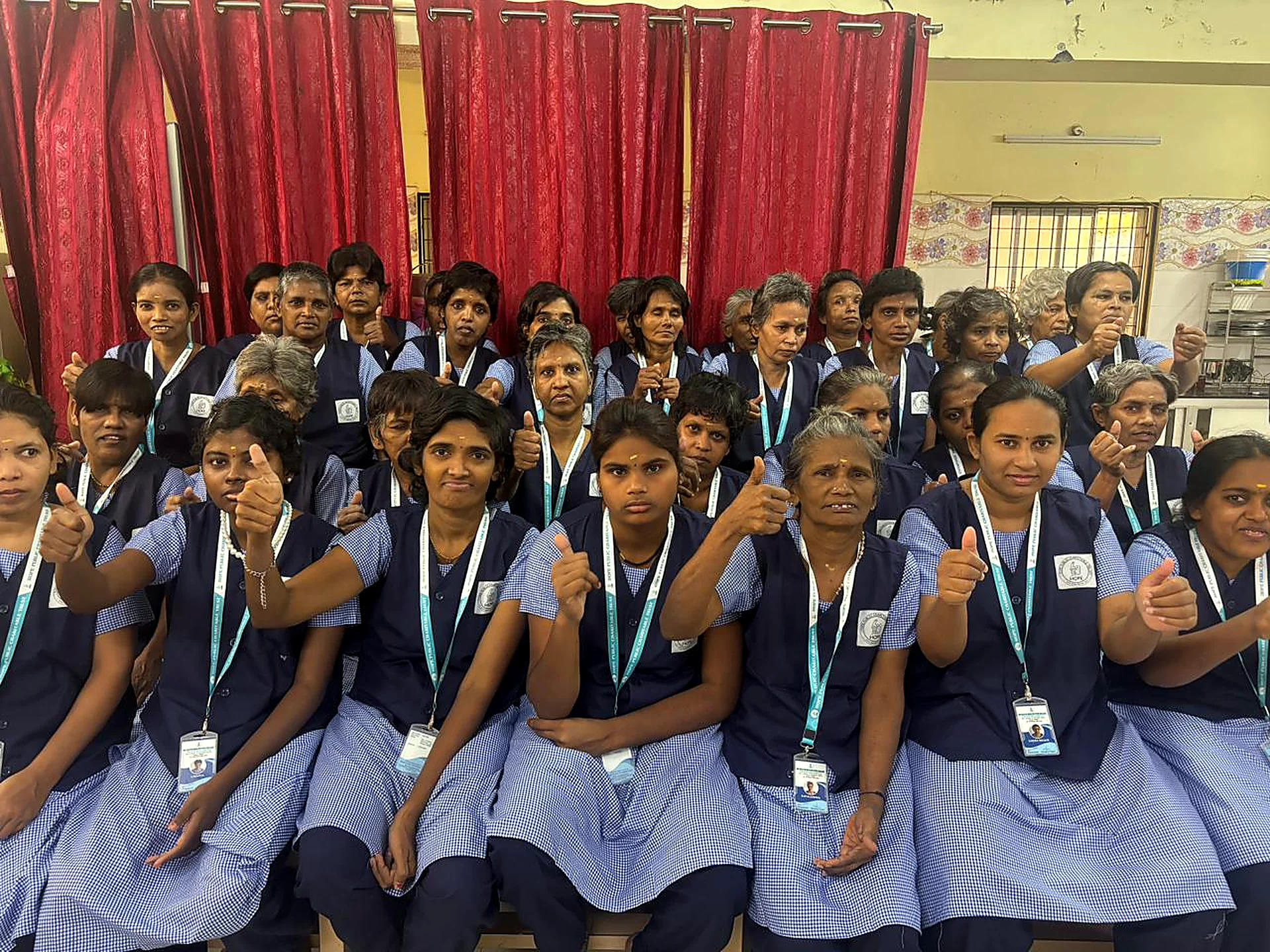 Women at Hope Chennai in uniform, seated together and giving a thumbs up